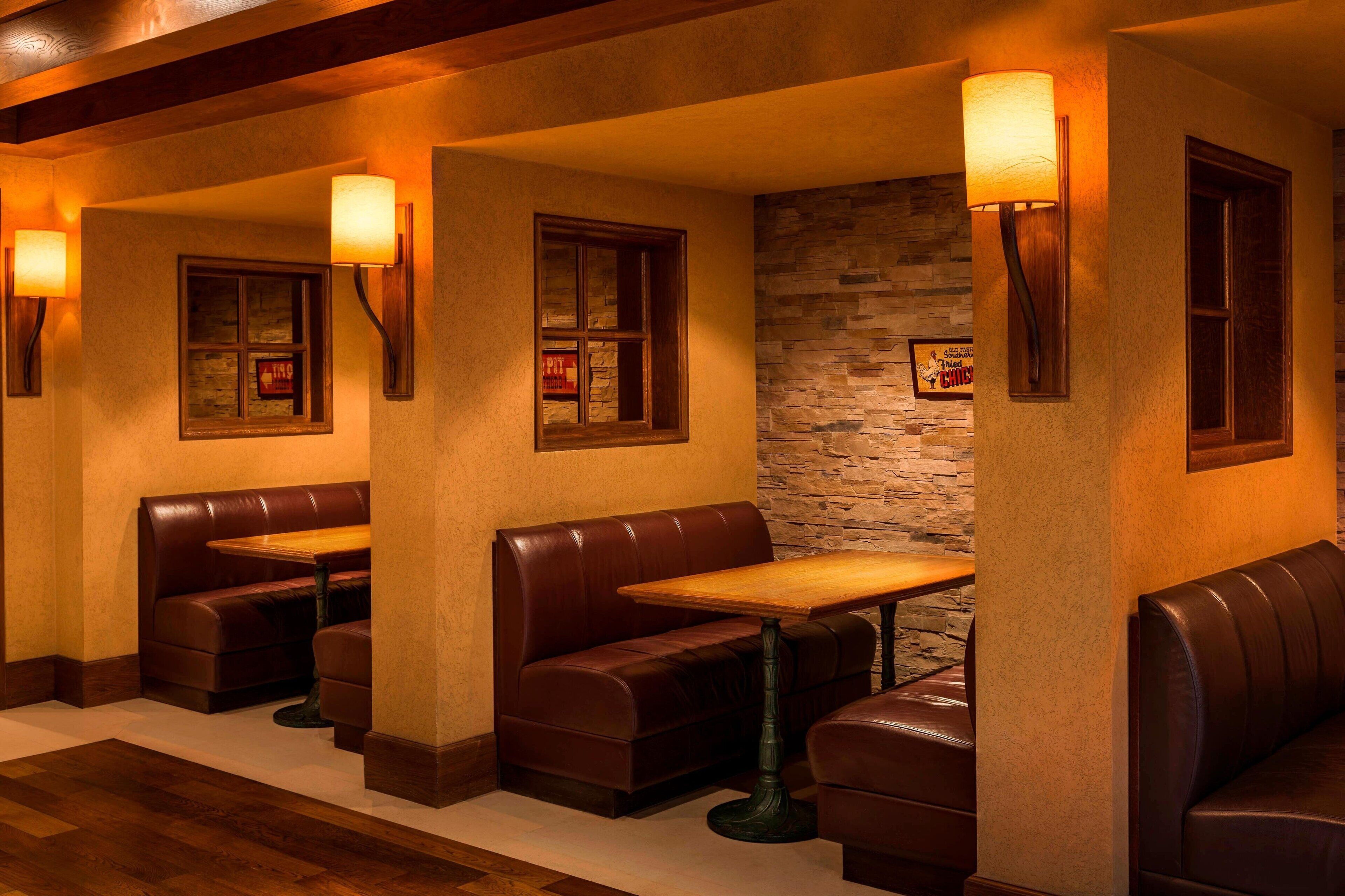 A restaurant with leather booths and tables, stone wall accents, and wall-mounted lamps.