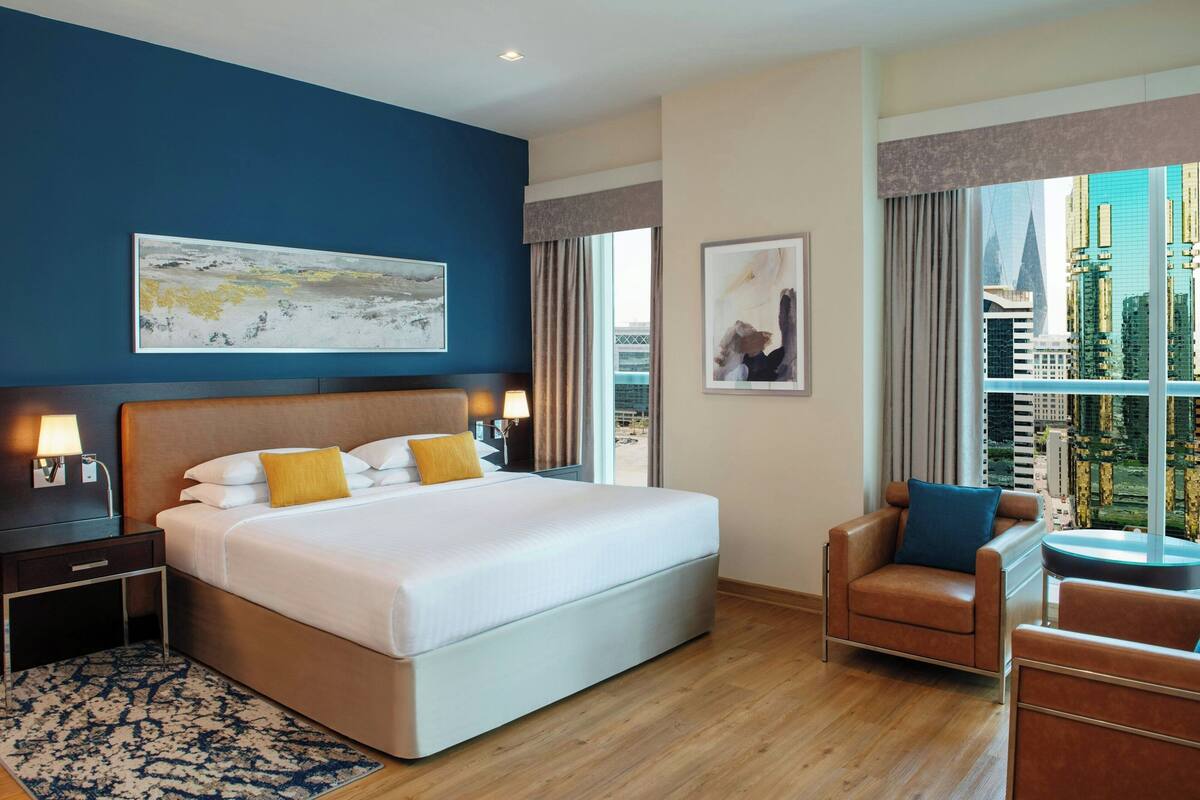 A modern hotel room with a large bed, a seating area, and a city view.