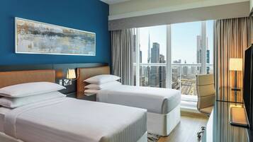 A hotel room with two beds, a desk, a chair, and a large window with a city view.
