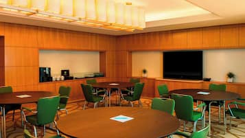 Un salón de conferencias con paneles de madera, sillas verdes y una amplia televisión de pantalla plana.