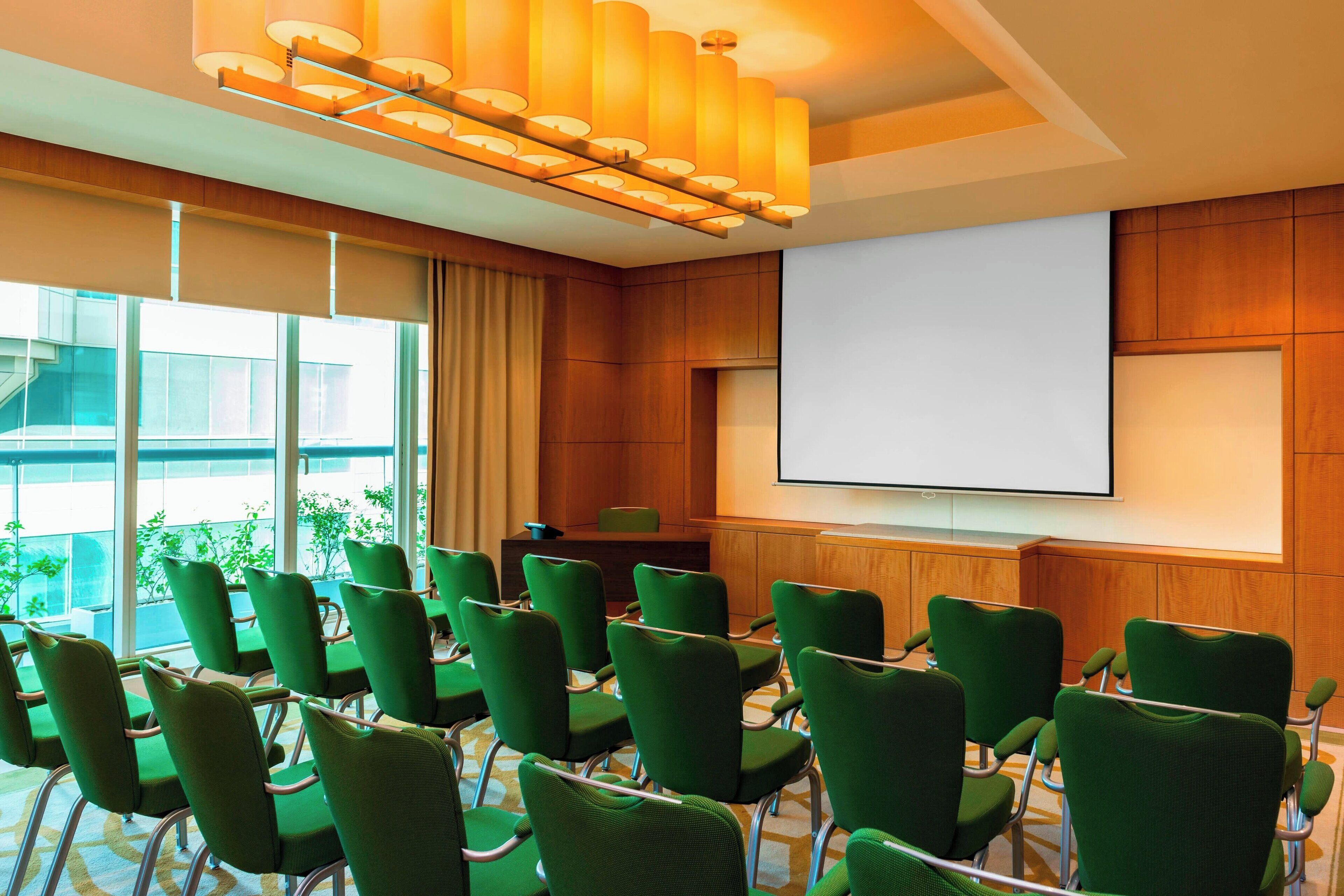 A conference room with green chairs, a large screen, and a wooden panel wall.