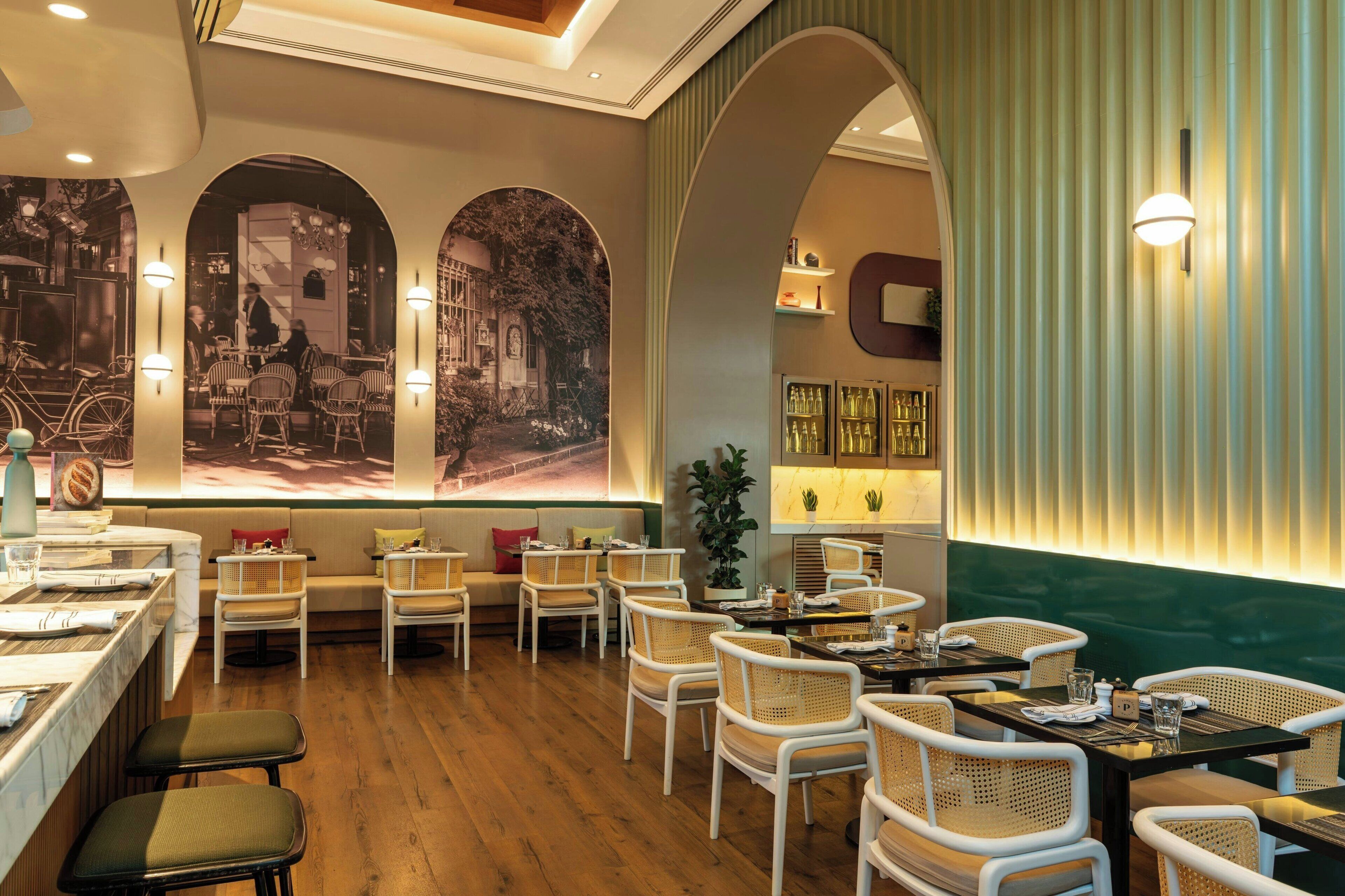 A restaurant with wooden floors, white wicker chairs, and a mural of a street scene.