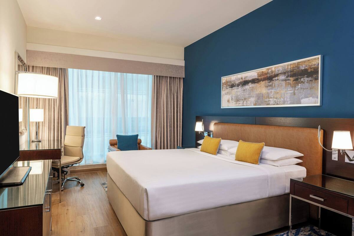A hotel room with a large bed, a desk with a chair, a TV, and a painting on the wall.