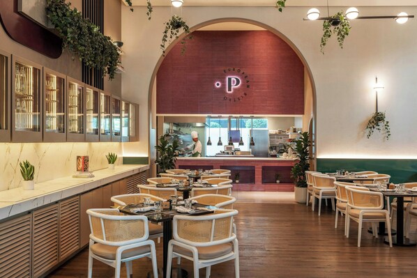 A restaurant with a modern interior, featuring a marble counter, wicker chairs, and a visible kitchen area.