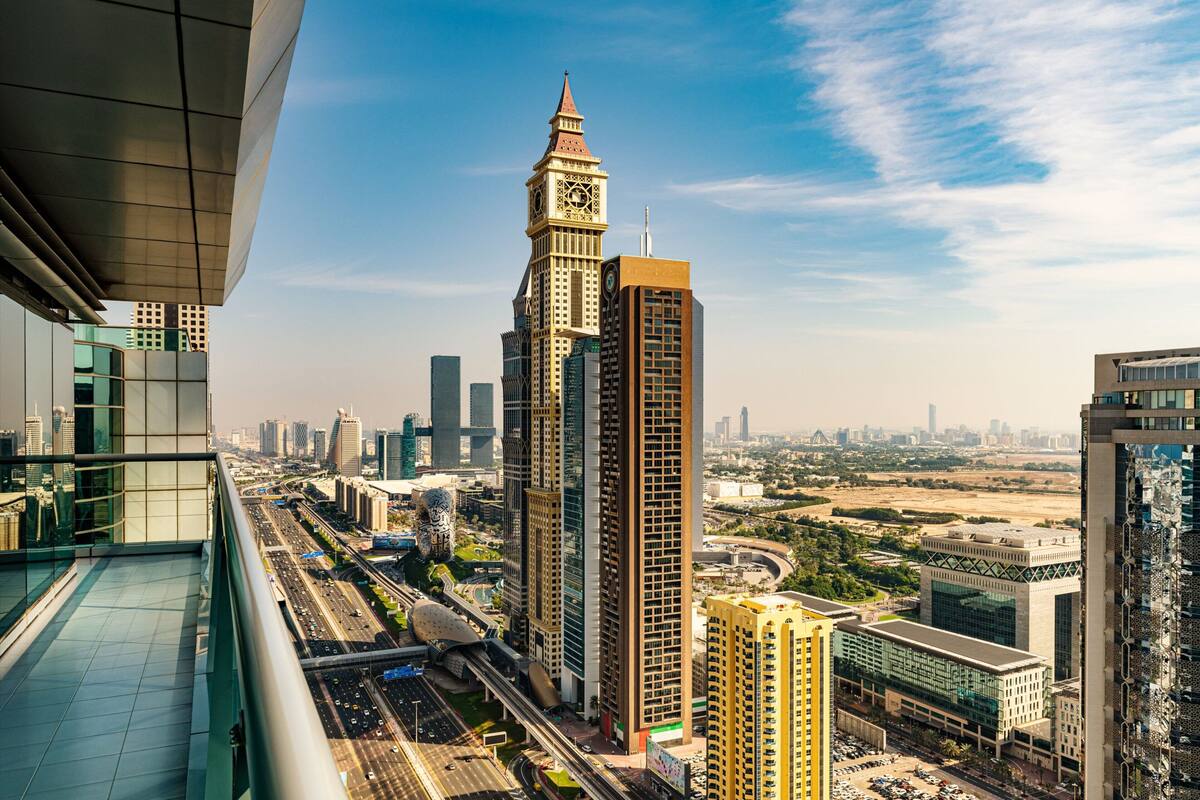 A high-rise building with a clock tower, surrounded by modern skyscrapers and a busy highway.