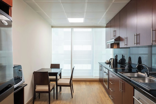 A modern kitchen with wooden cabinets, a stainless steel sink, and a dining area with a table and chairs. - Four Points by Sheraton Sheikh Zayed Road, Dubai (Dubai)