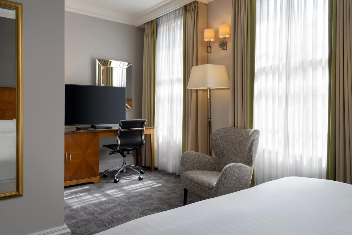 A hotel room with a bed, a desk with a computer, a chair, a TV, and curtains.