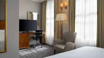 Habitación de hotel con cama, escritorio con computadora, silla, televisor y cortinas.