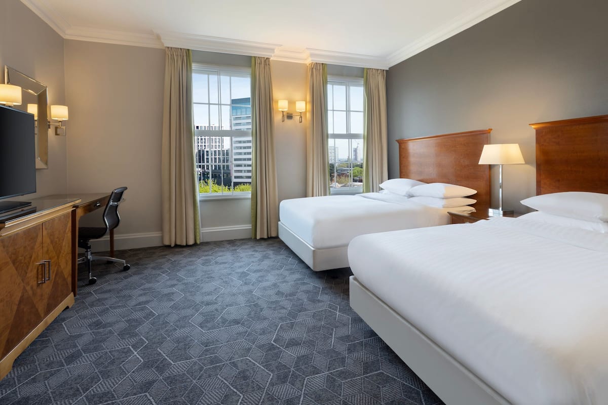 A hotel room with two beds, a desk, a TV, and a window with curtains.