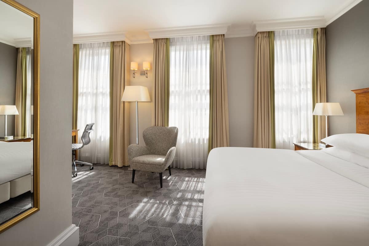 A hotel room with a large bed, a chair, a desk, and a mirror.