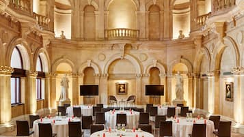 Un salón amplio con varias mesas redondas dispuestas para comer, detalles arquitectónicos ornamentados y estatuas.