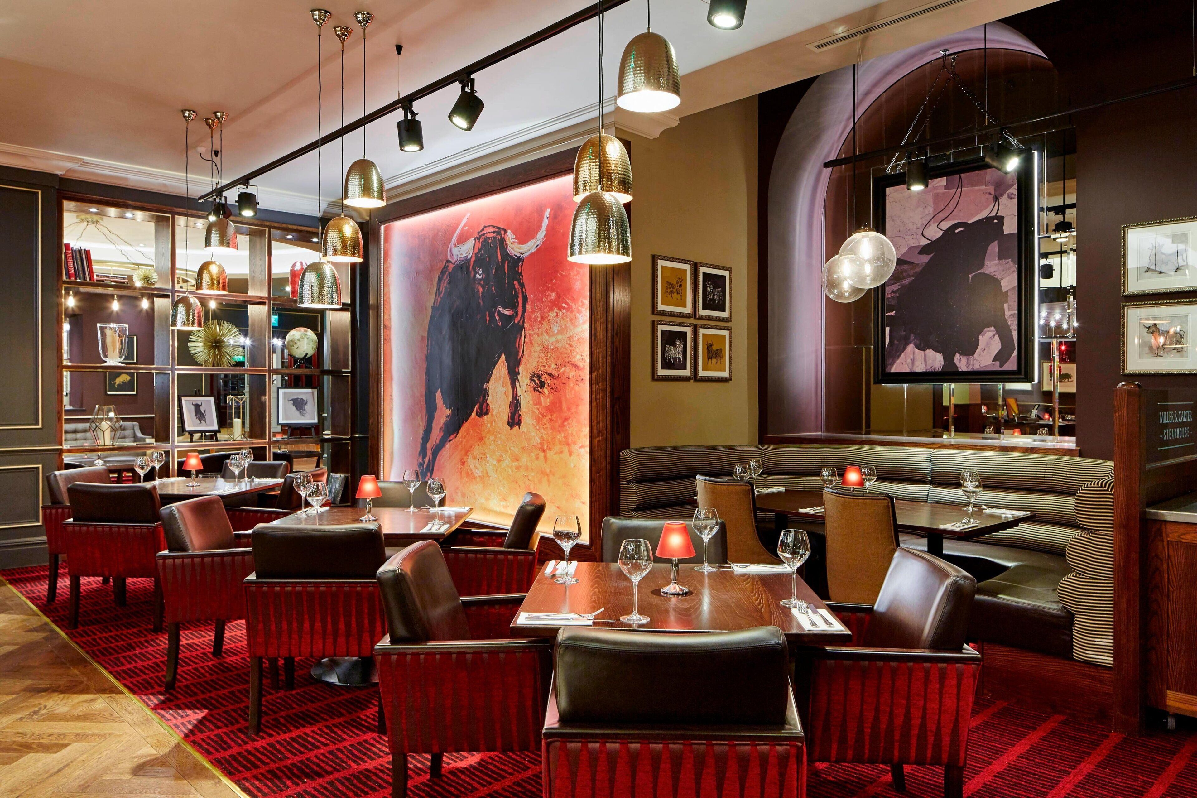 A restaurant with red carpet flooring, leather seating, and pendant lighting.