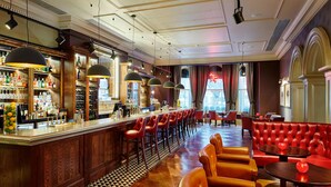 A bar area with a checkered floor, wooden bar counter, and red upholstered seating.