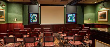 A conference room with a large screen, green walls, and rows of folding chairs.