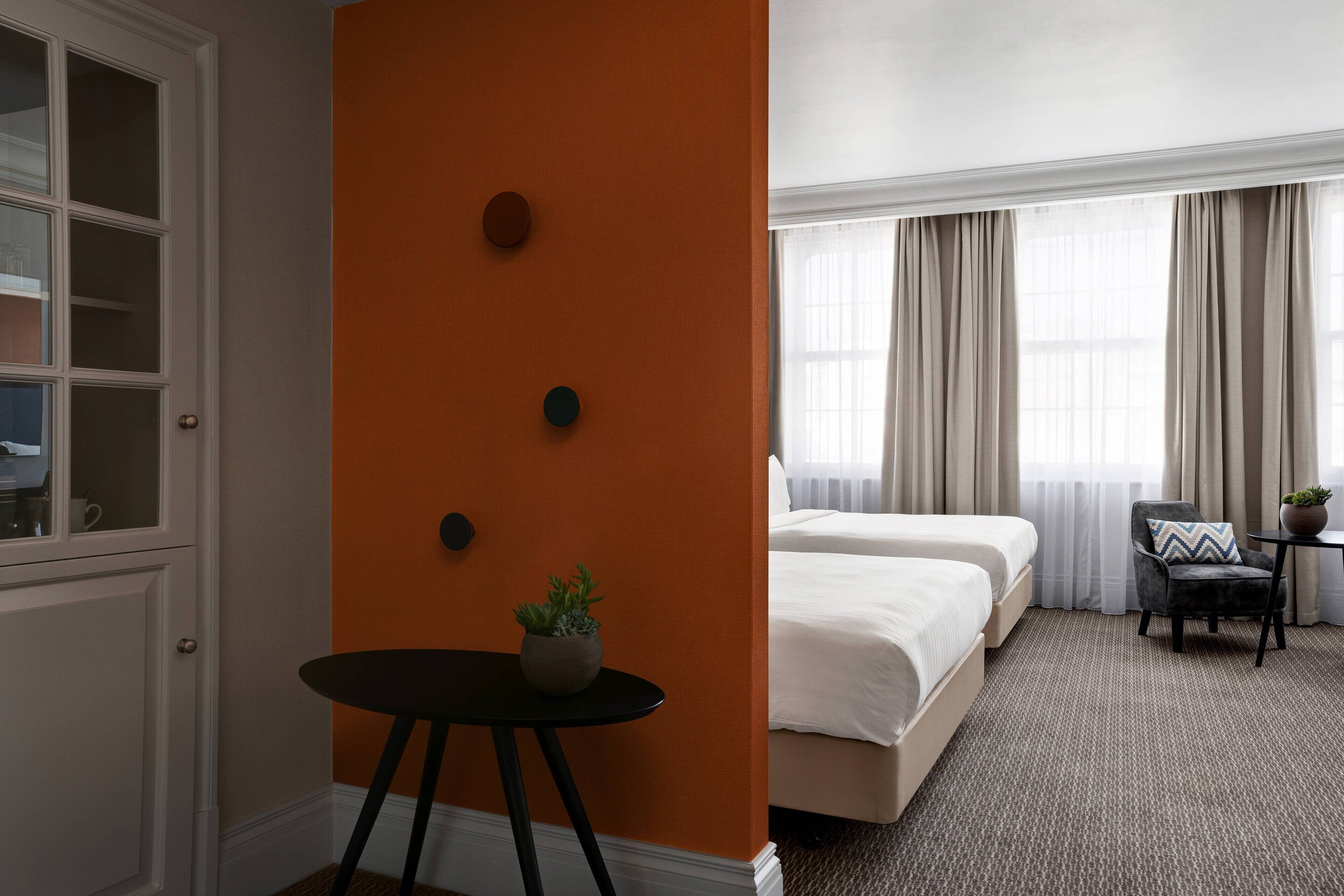 Une chambre d’hôtel avec un lit, une petite table sur laquelle se trouve une plante, une chaise et une fenêtre avec des rideaux.