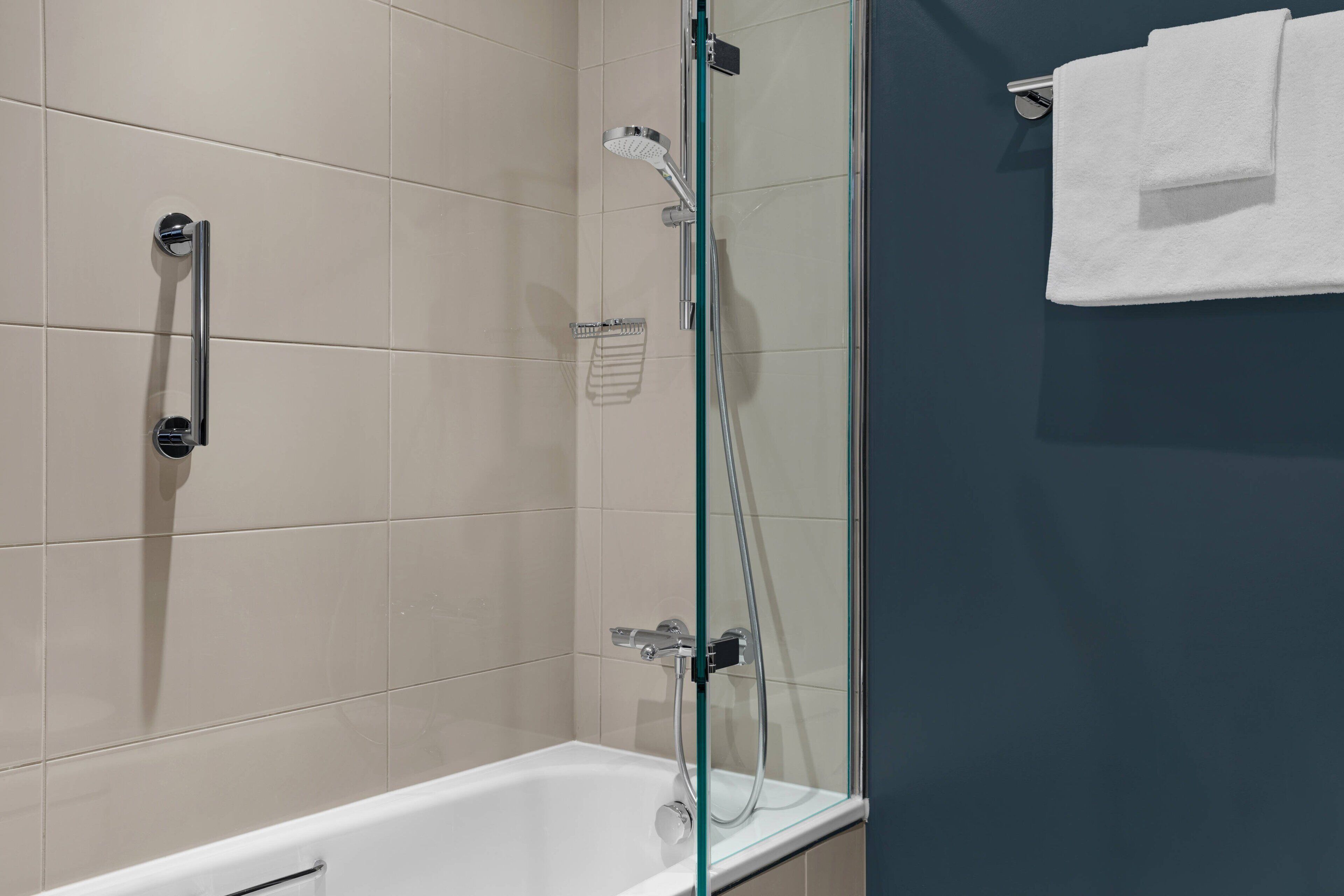 A modern bathroom with a glass-enclosed shower, a white bathtub, and a towel rack.