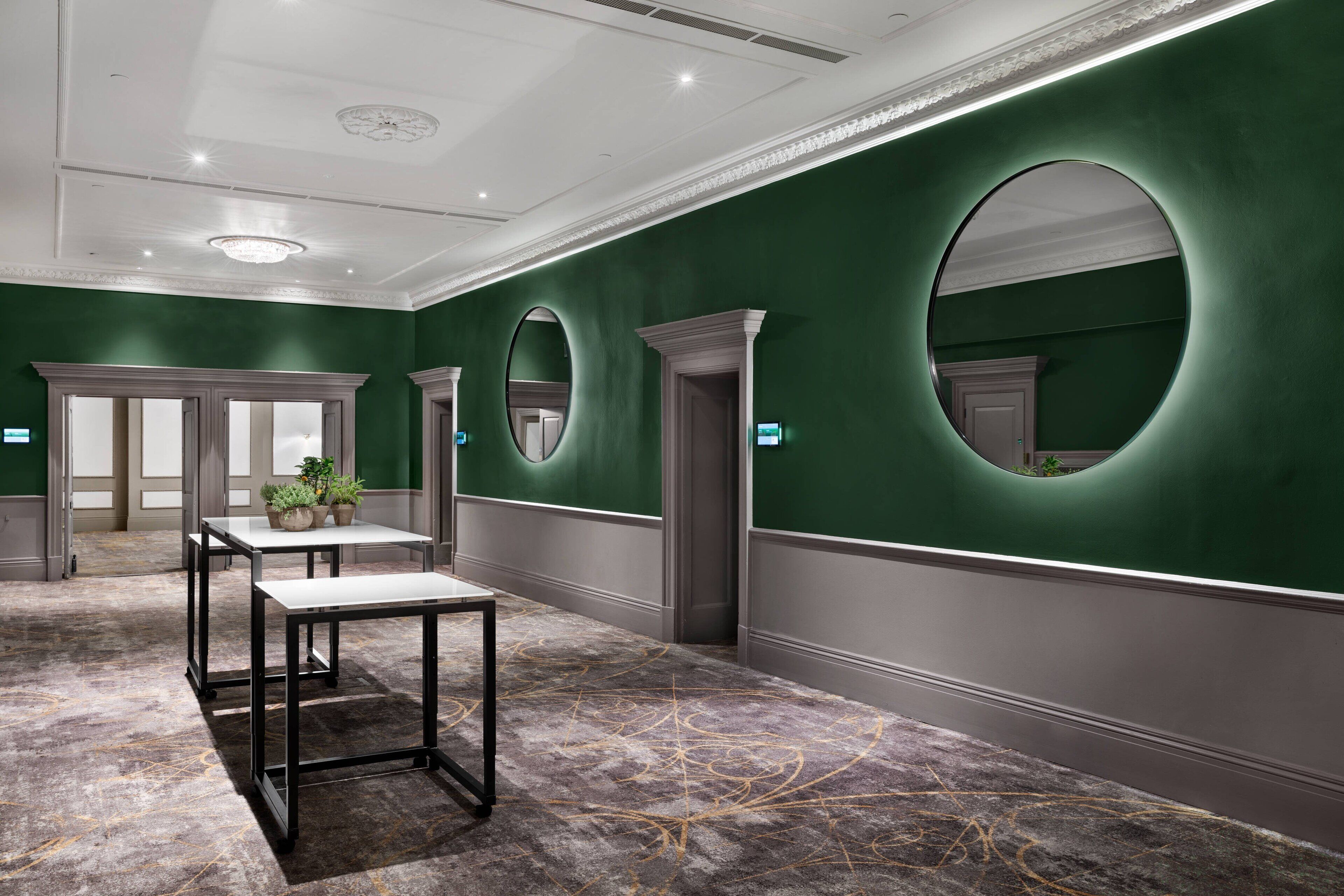 En modern hotellobby med gröna väggar, stora speglar och ett marmorgolv.