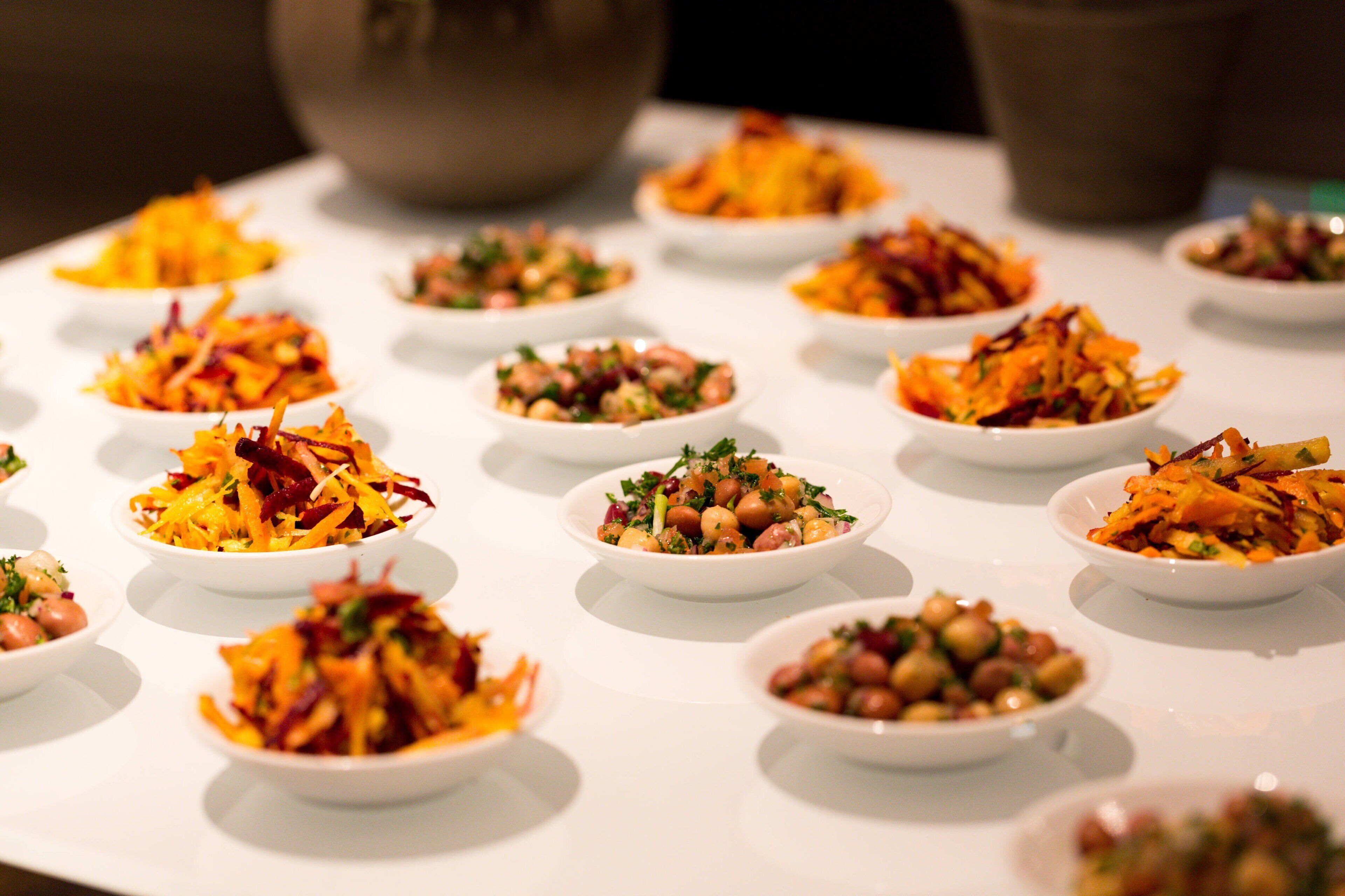A table with multiple small white bowls containing various salads.