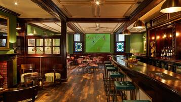 Eine Bar mit Holzboden, Barhocker und einem großen Bildschirm, der ein Fußballspiel zeigt.