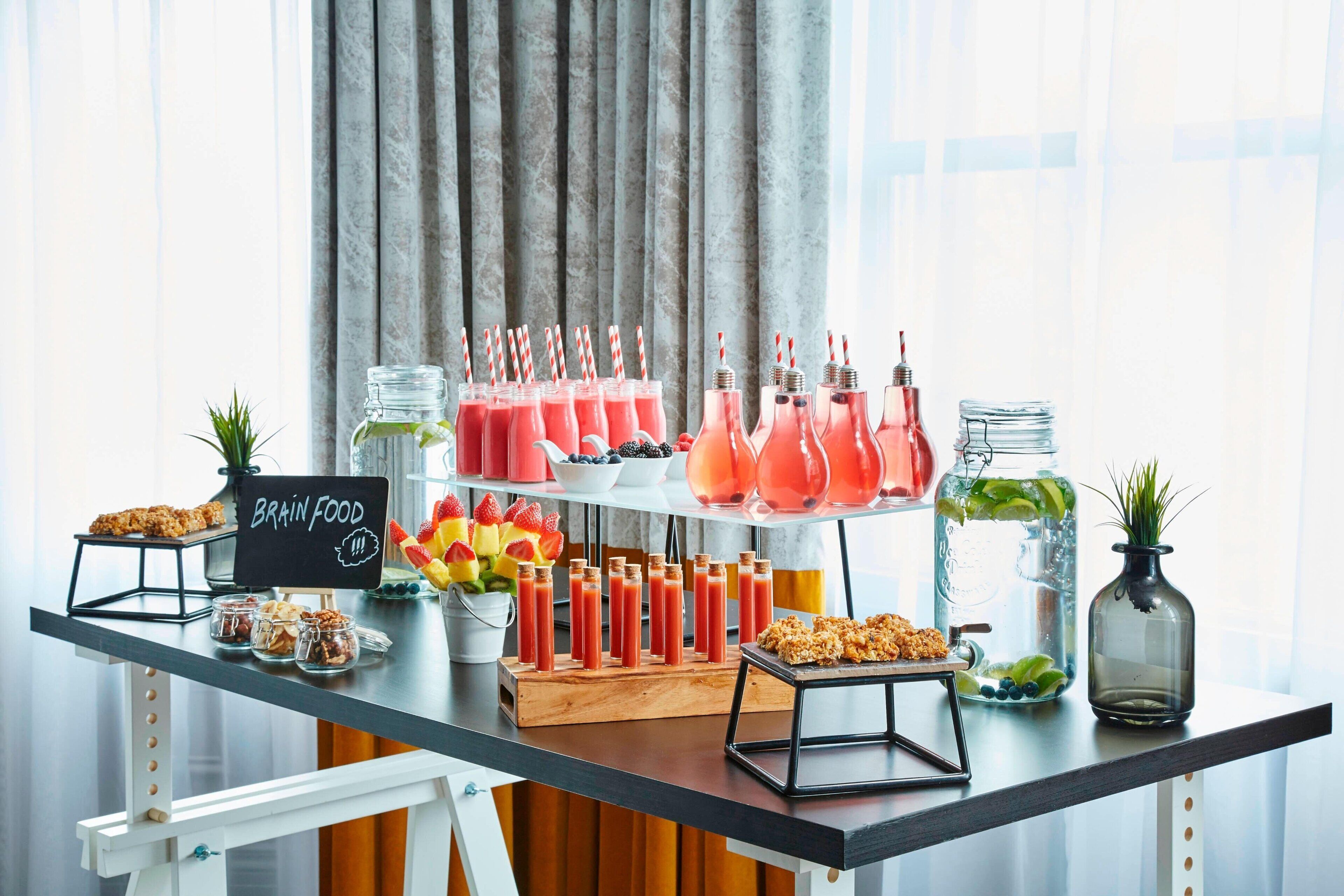 Une table de buffet proposant une variété d’aliments et de boissons, notamment des smoothies et des fruits, ainsi qu’un panneau indiquant « Aliments pour le cerveau ».