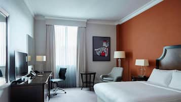 A hotel room with a large bed, a desk with a chair, a small table, and a TV.