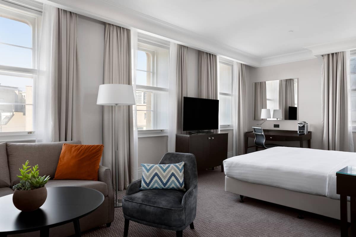 A hotel room with a bed, a sofa, a chair, a desk, a television, and a window with curtains.
