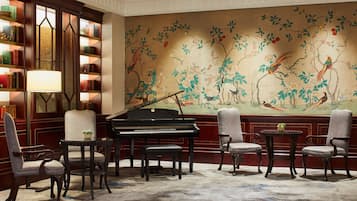 A room with a grand piano, a bookshelf, and a mural with birds and flowers.