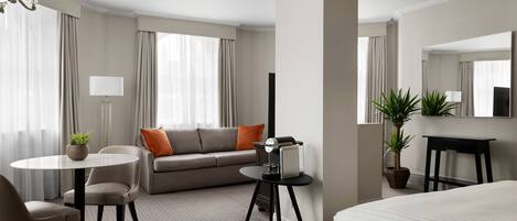 A modern hotel room with a bed, a sofa, a dining table, and a small side table.