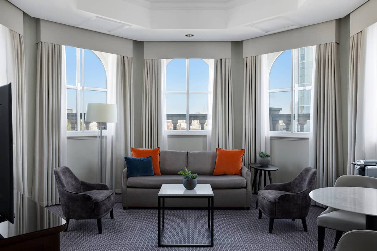 A hotel room with a grey sofa, two armchairs, a small table with a plant, and a TV.