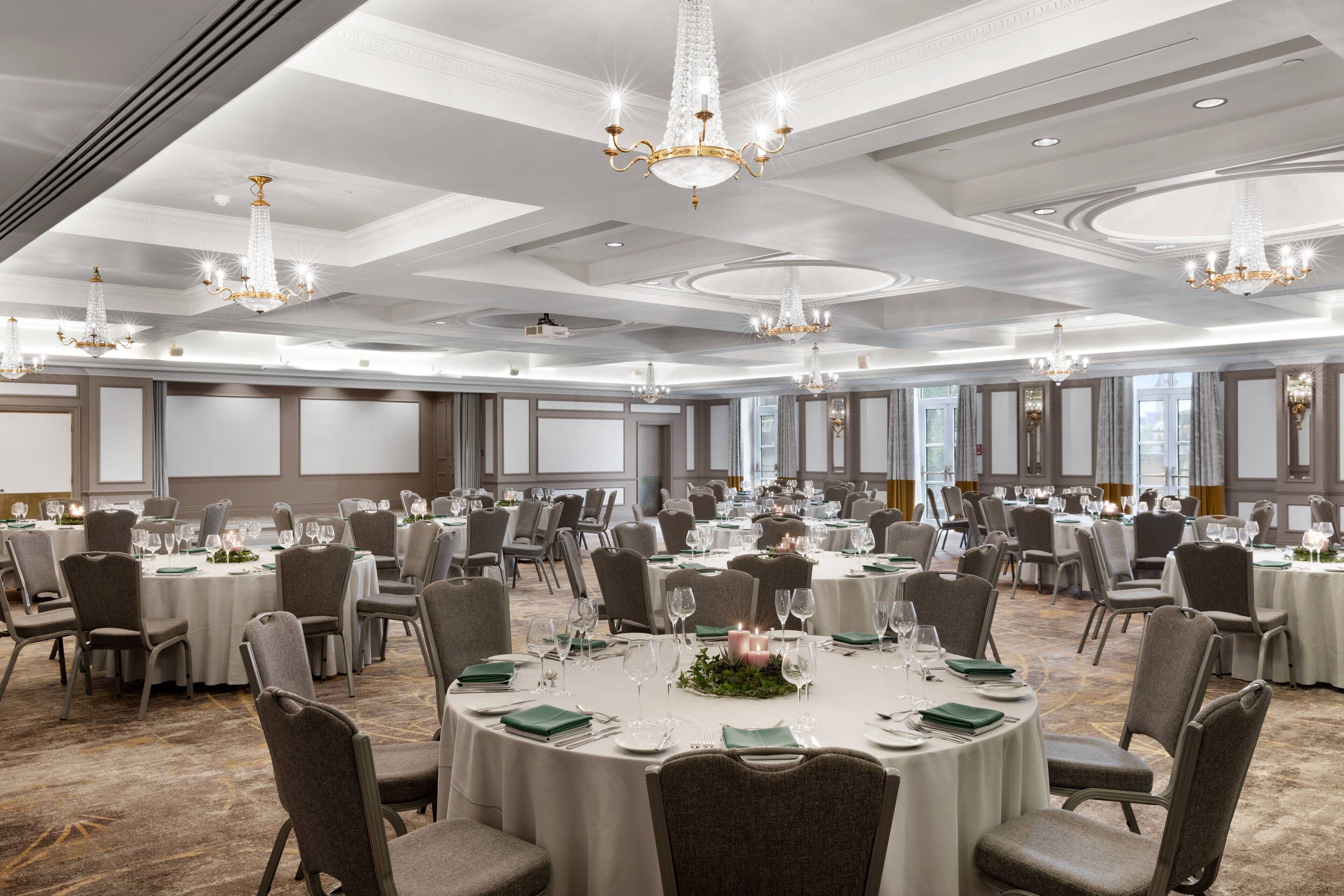 Un gran salón de banquetes con mesas redondas, sillas, candelabros y suelo alfombrado.