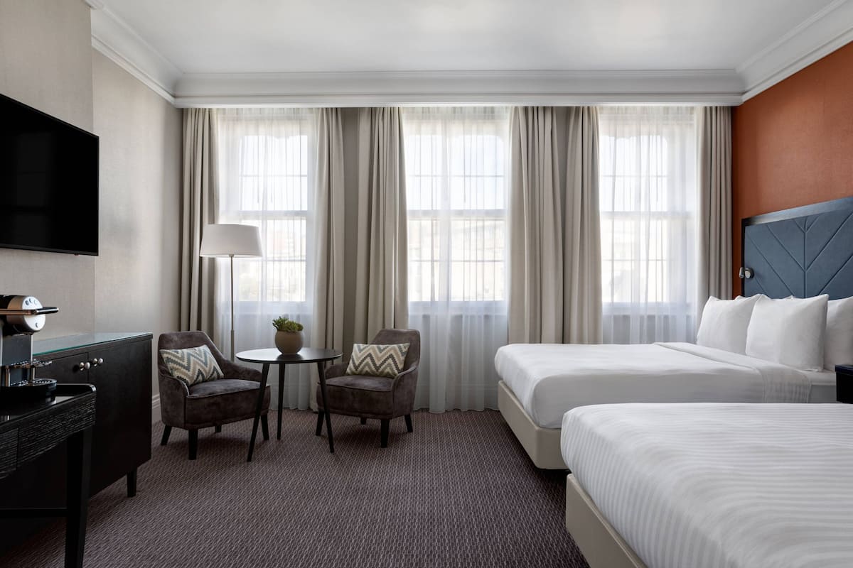 A hotel room with two beds, a TV, a desk, and a chair.