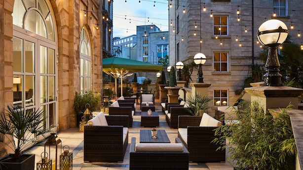 An outdoor seating area with wicker furniture, a green umbrella, and string lights.