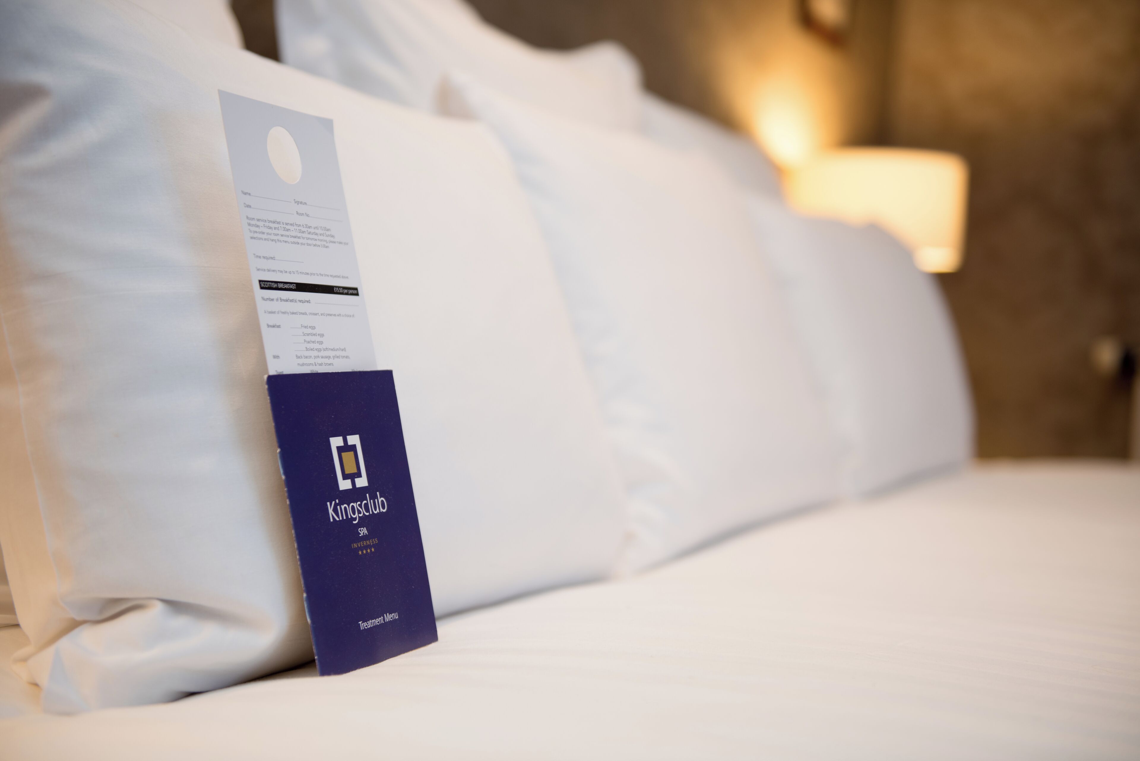 A hotel bed with white linens and a Kings Club membership card on the side.