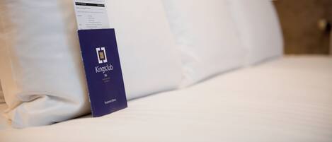 A hotel bed with white linens and a Kings Club membership card on the side.
