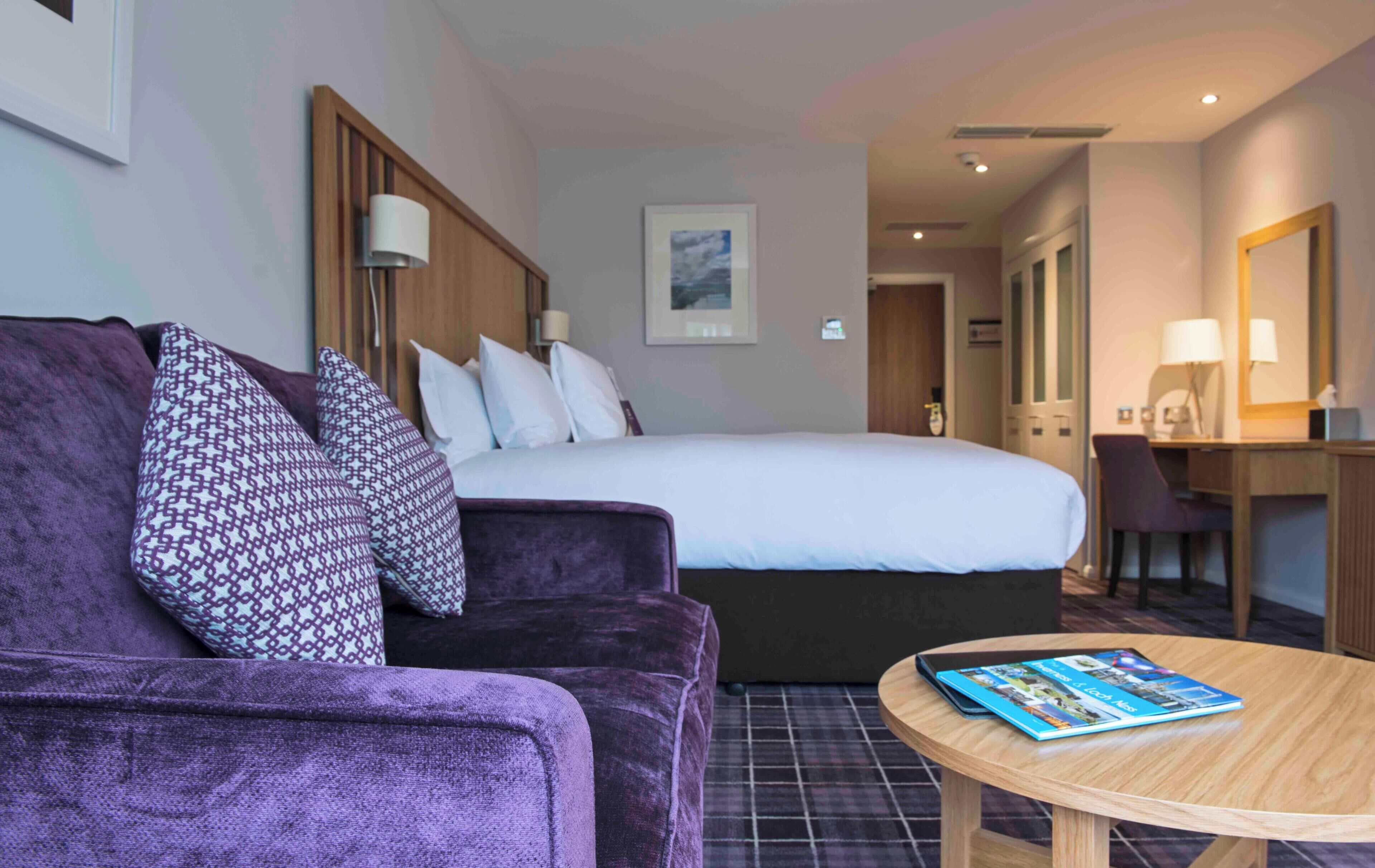 A hotel room with a bed, a sofa, a desk, and a round table.