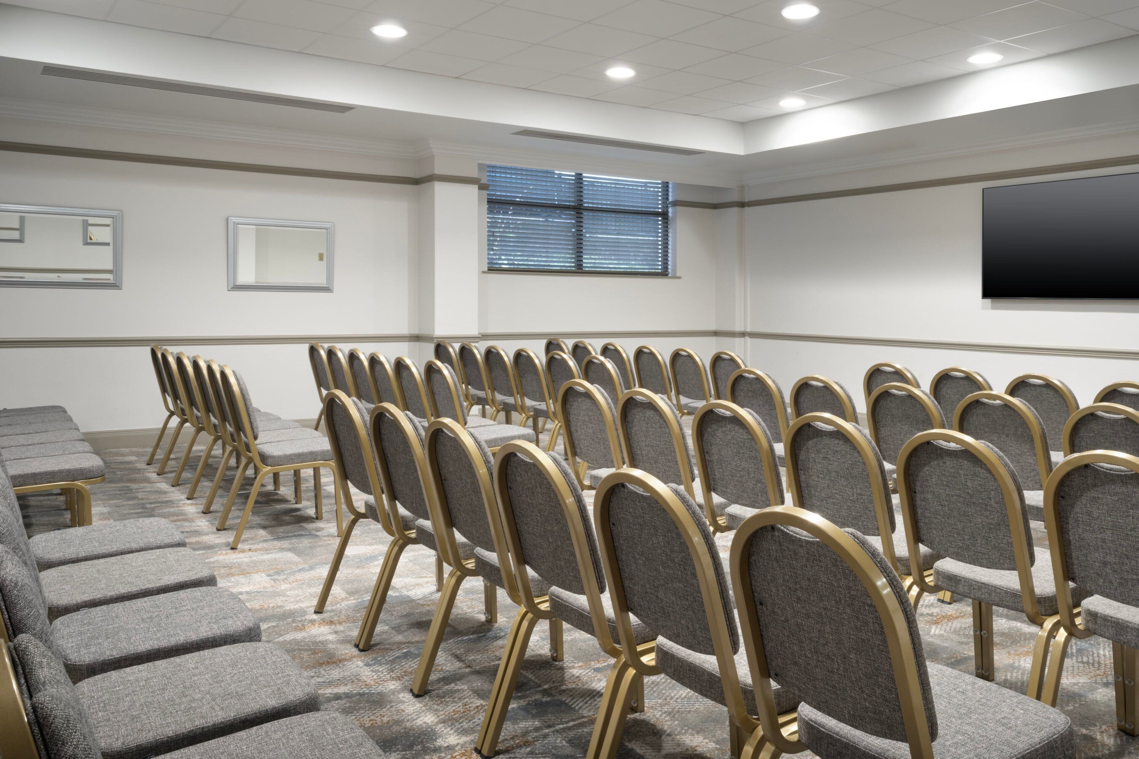 A conference room with rows of grey upholstered chairs and a long table.