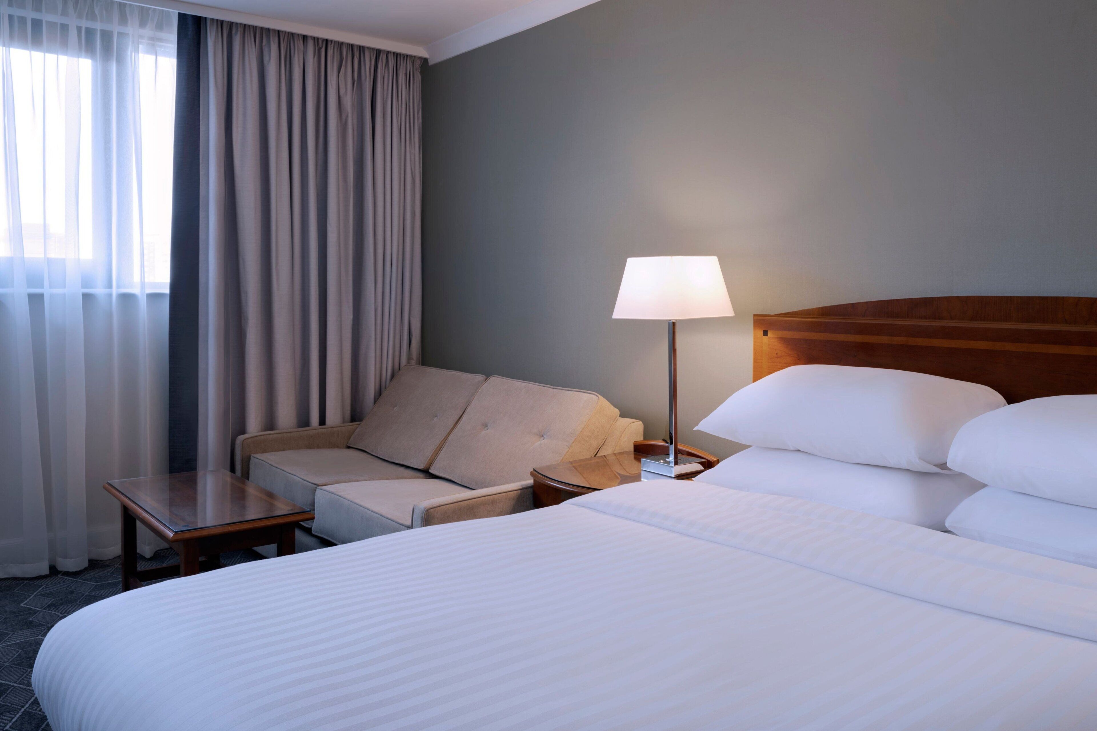 A hotel room with a large bed, a sofa, a table, and a lamp.