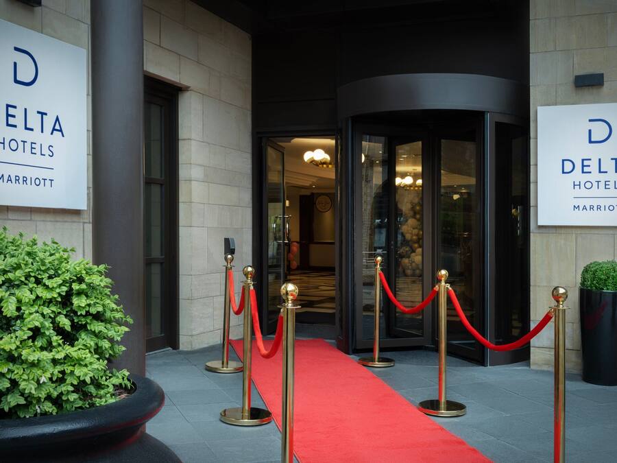 The entrance of a Delta Hotels Marriott with a red carpet and gold stanchions.