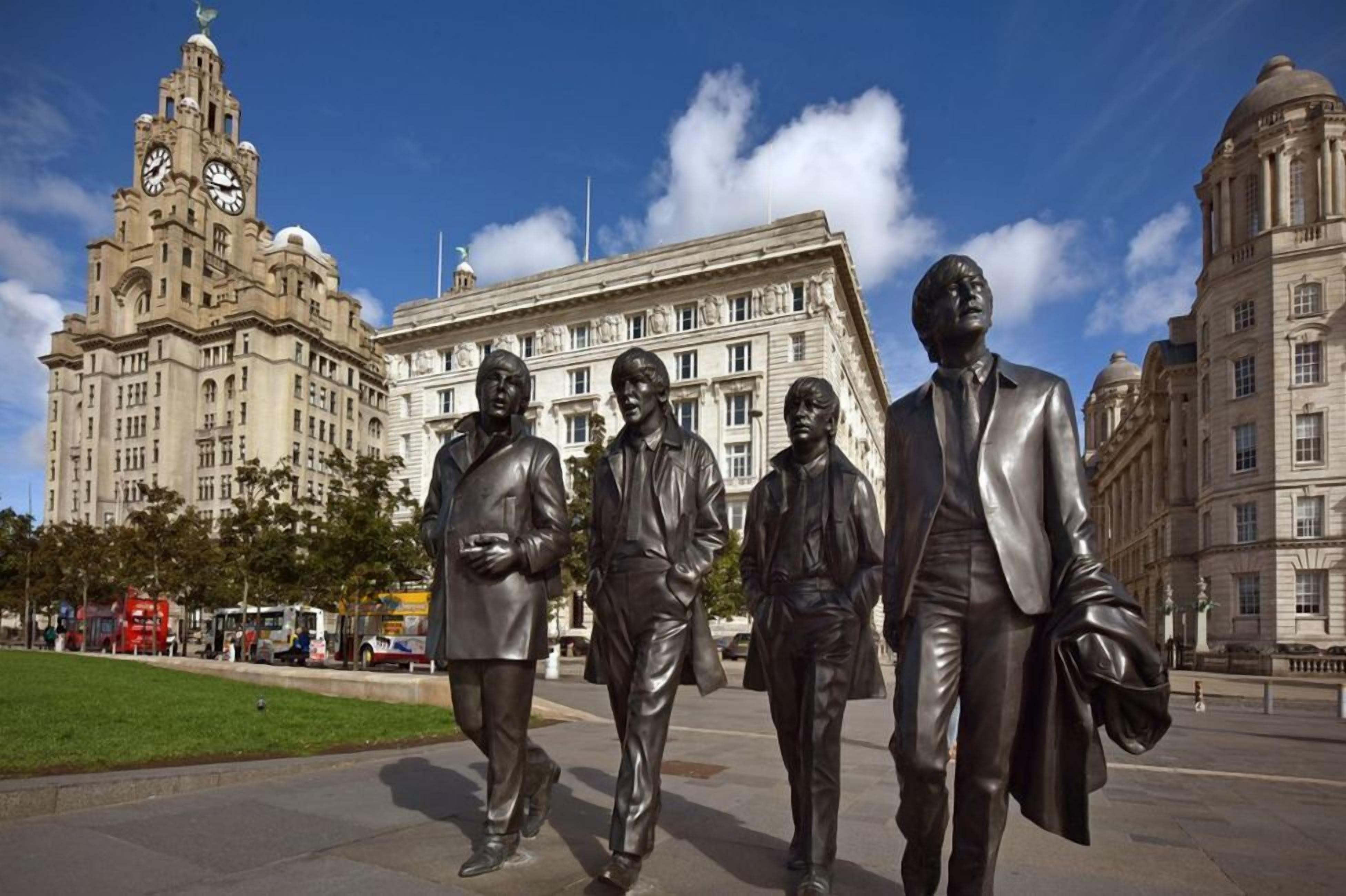 A statue of four men in suits on a city square with historic buildings in the background.