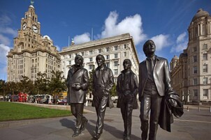 Una estatua de cuatro hombres con traje en una plaza de la ciudad con edificios históricos al fondo.