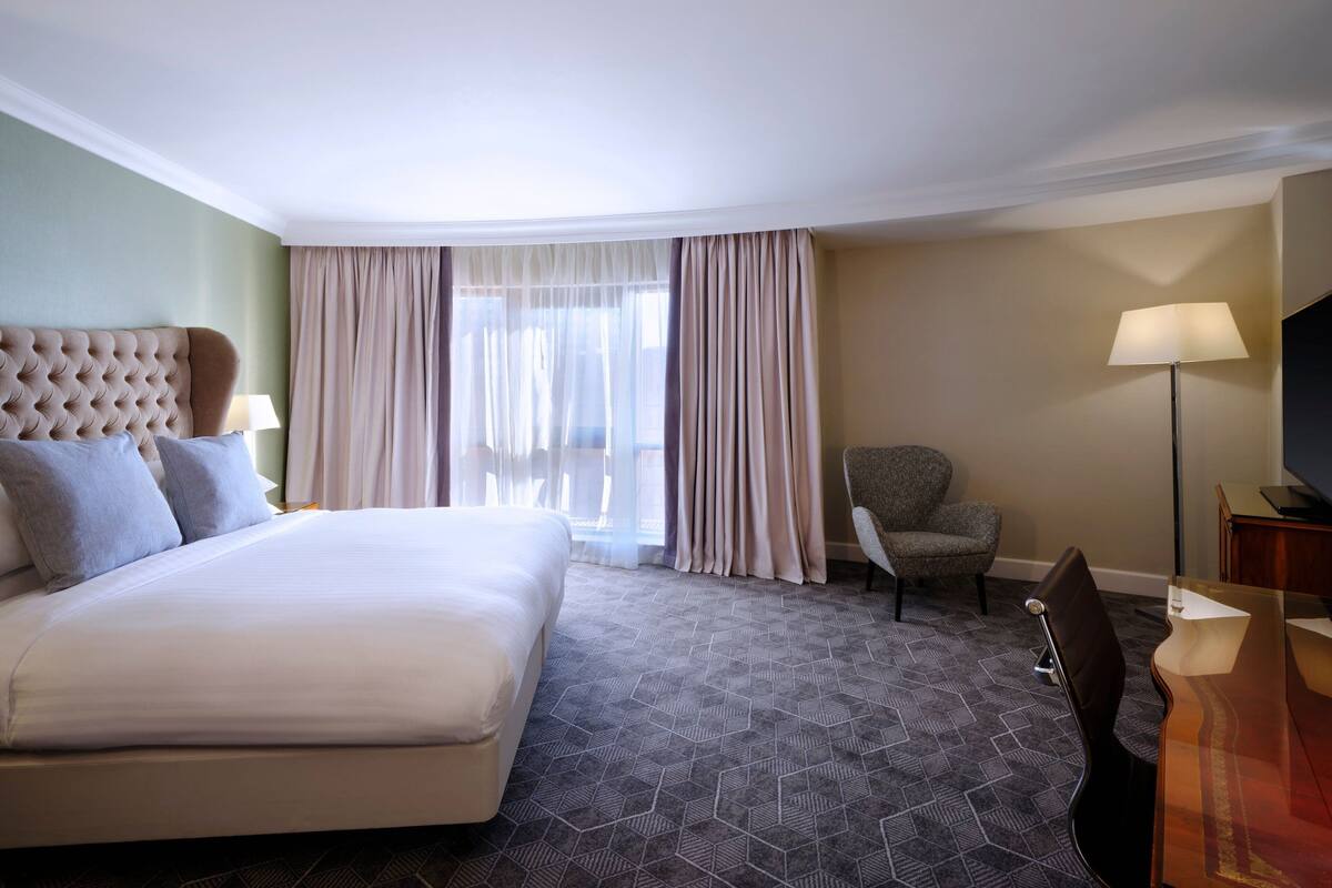 A hotel room with a large bed, a chair, a desk, and a lamp.