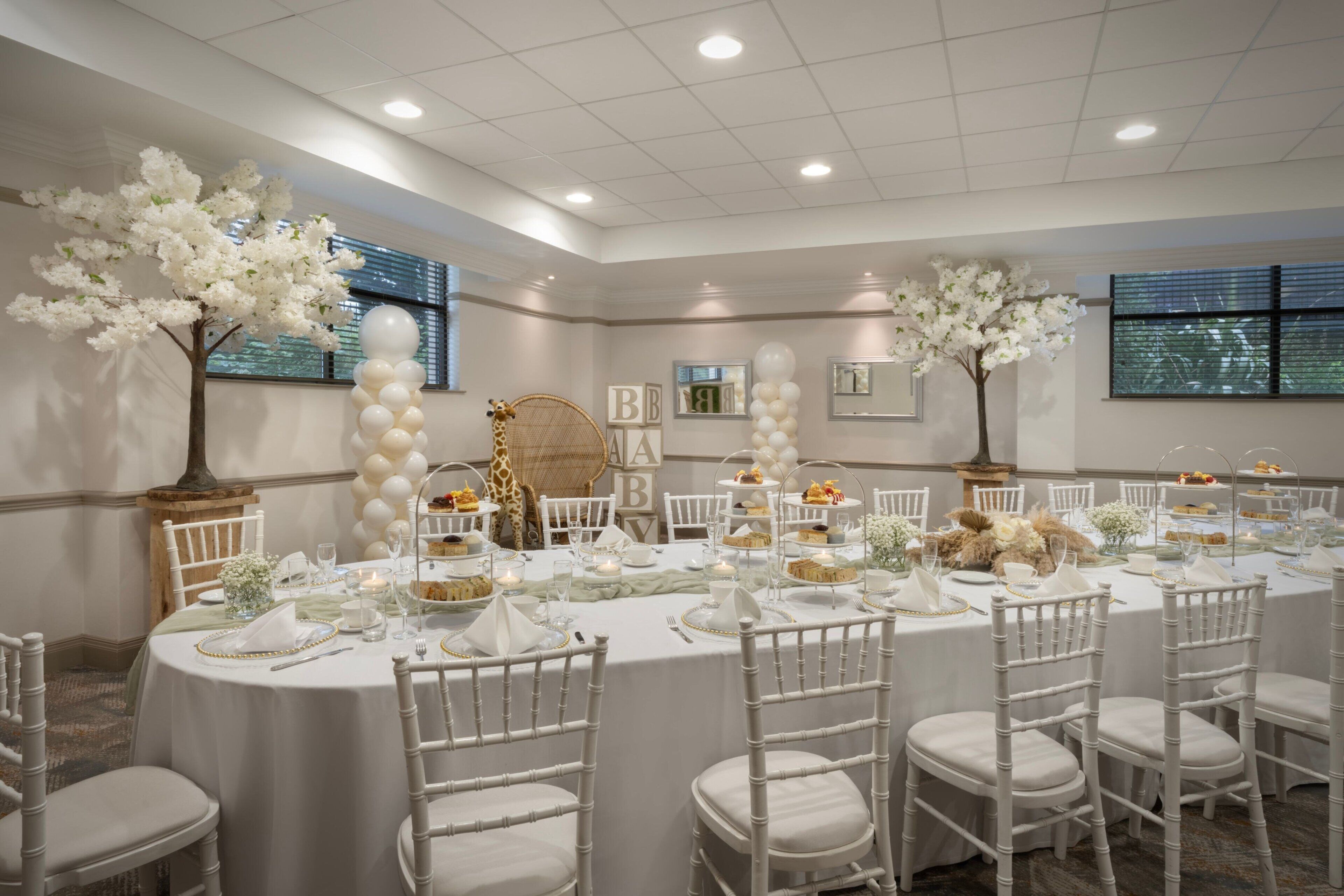 A banquet hall with round tables, white chairs, and floral decorations.