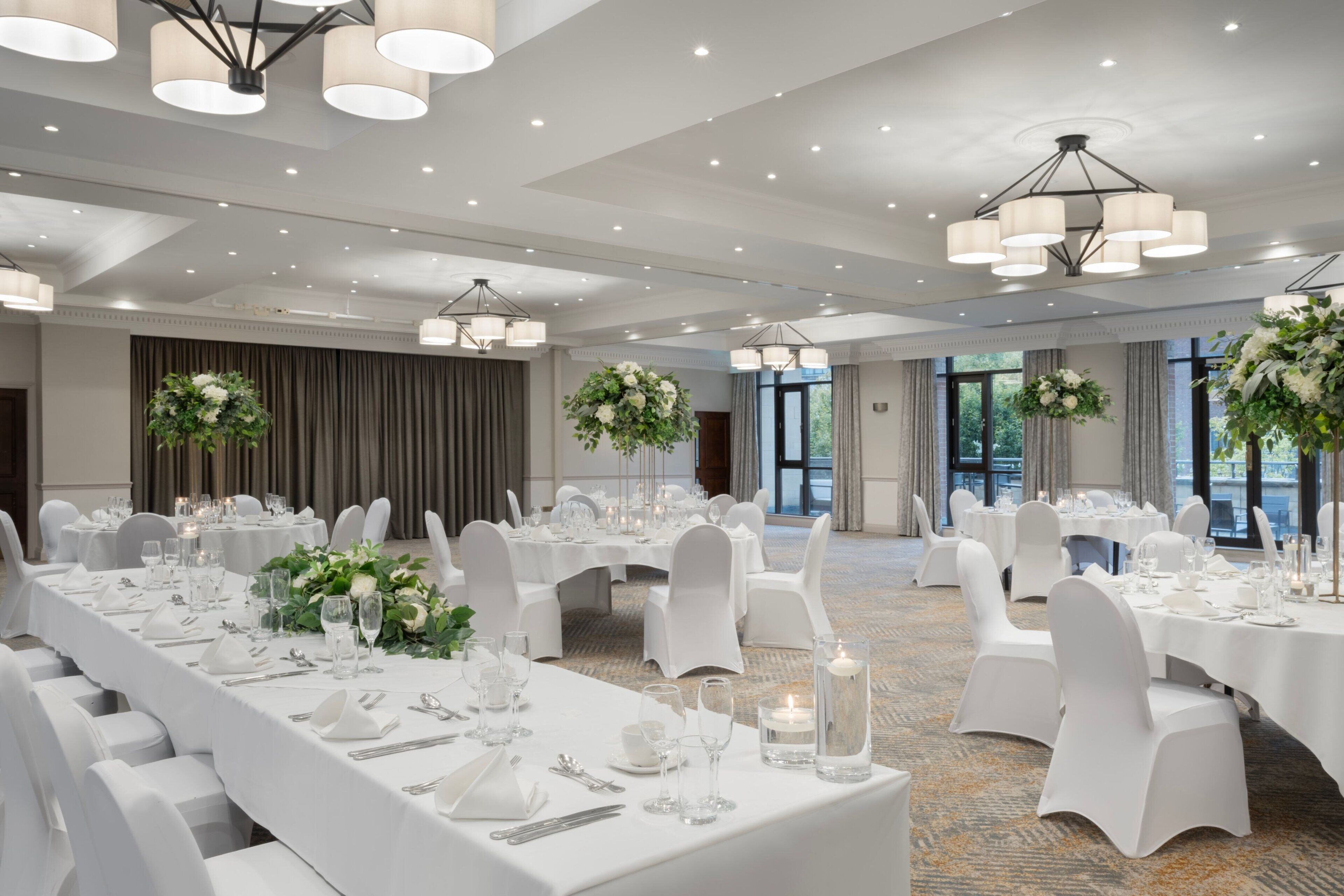 A banquet hall with round tables, white tablecloths, and floral centerpieces.