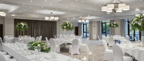 A banquet hall with round tables, white tablecloths, and floral centerpieces.