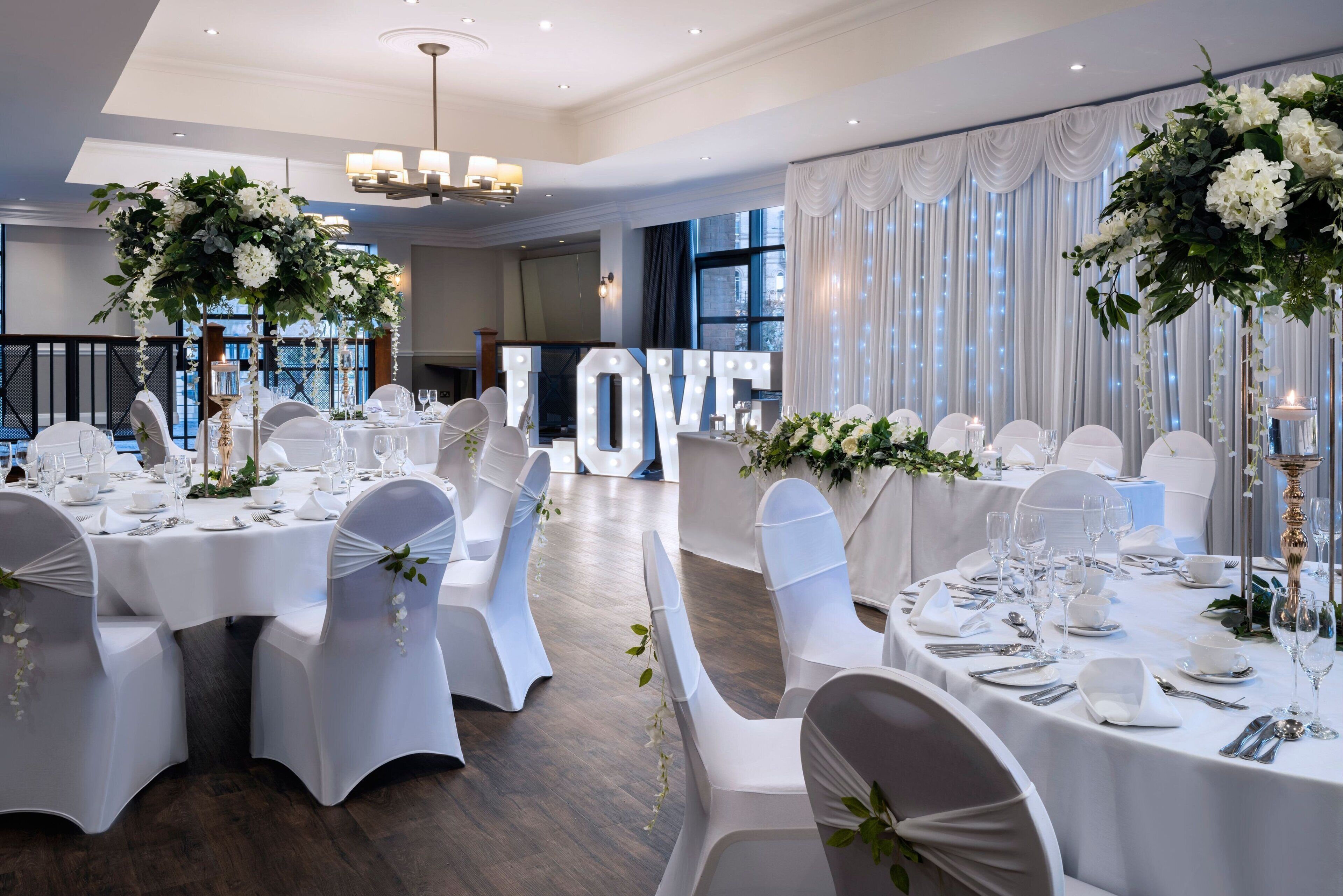 A banquet hall with round tables set for a formal event, featuring white tablecloths, chairs, and floral centerpieces.