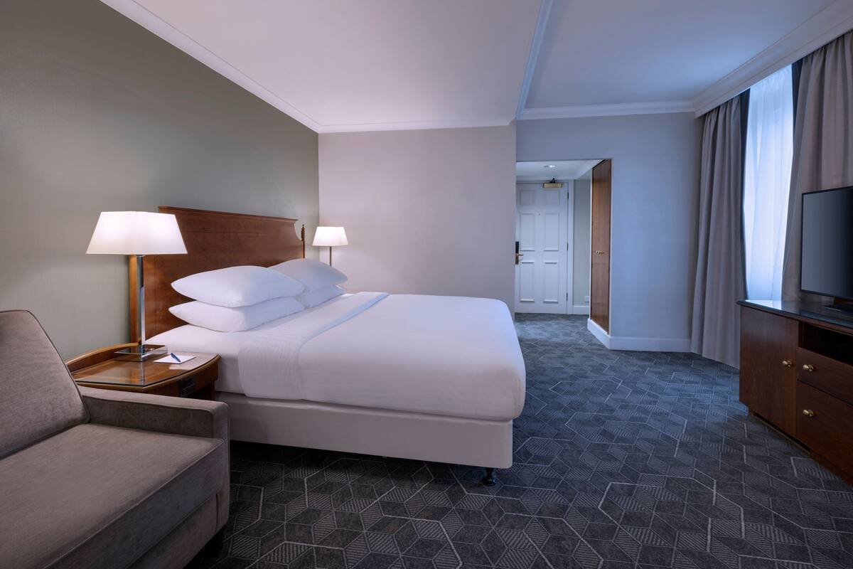 A hotel room with a bed, a sofa, a TV, and a lamp.