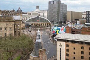 A cityscape with a prominent building featuring a large arched entrance and a clock tower.