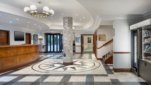 En hotellobby med en receptionsdisk, en kolonn med ett mönster, en trappa och en kyld utställningsdisk med texten ”CRAB & GO”.