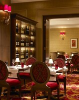 A dining area with a wine cellar, red upholstered chairs, and a patterned carpet.