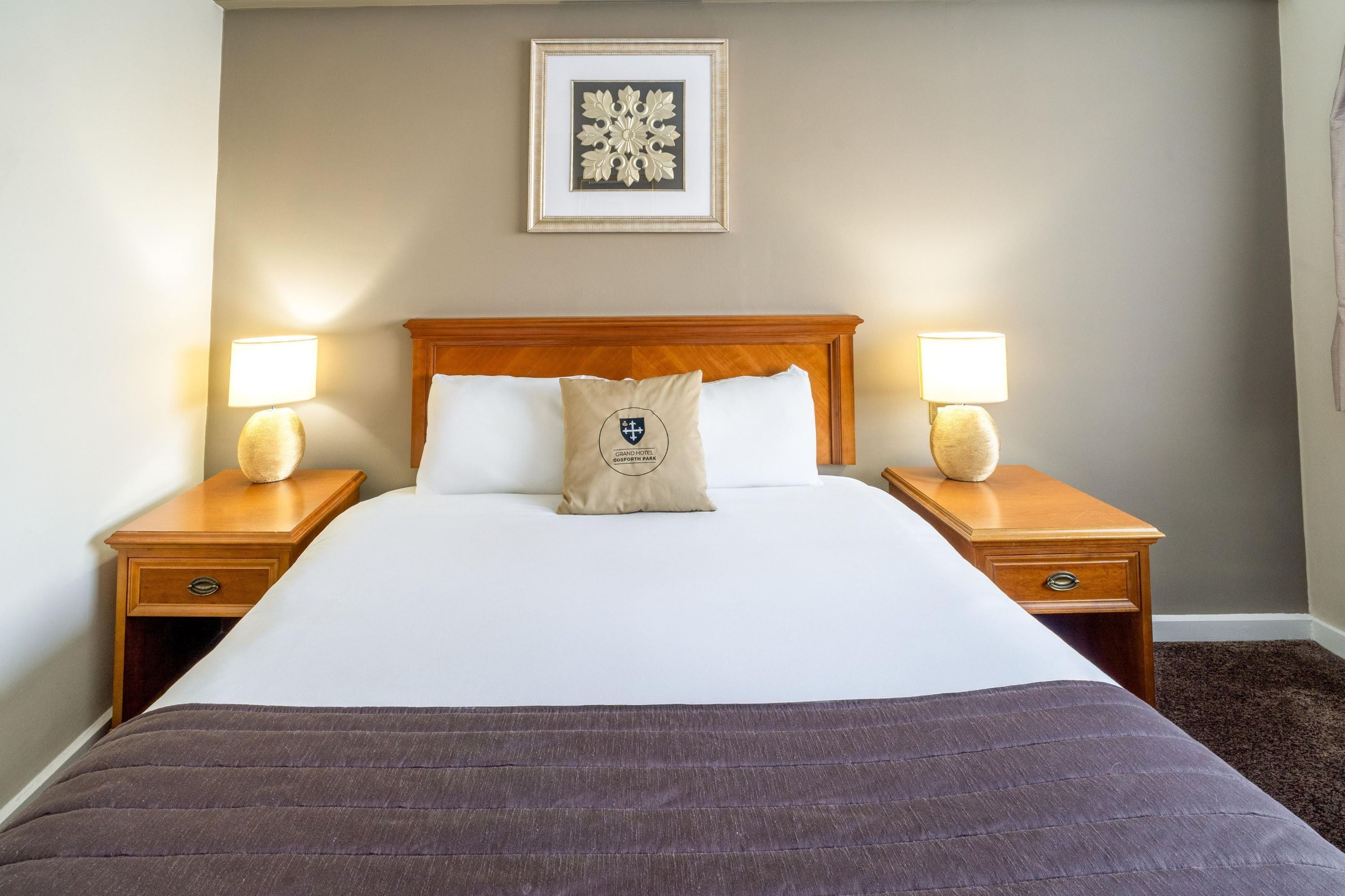 Une chambre d’hôtel avec un grand lit, deux tables de chevet avec des lampes, une œuvre d’art encadrée au-dessus du lit et un sol recouvert de moquette.